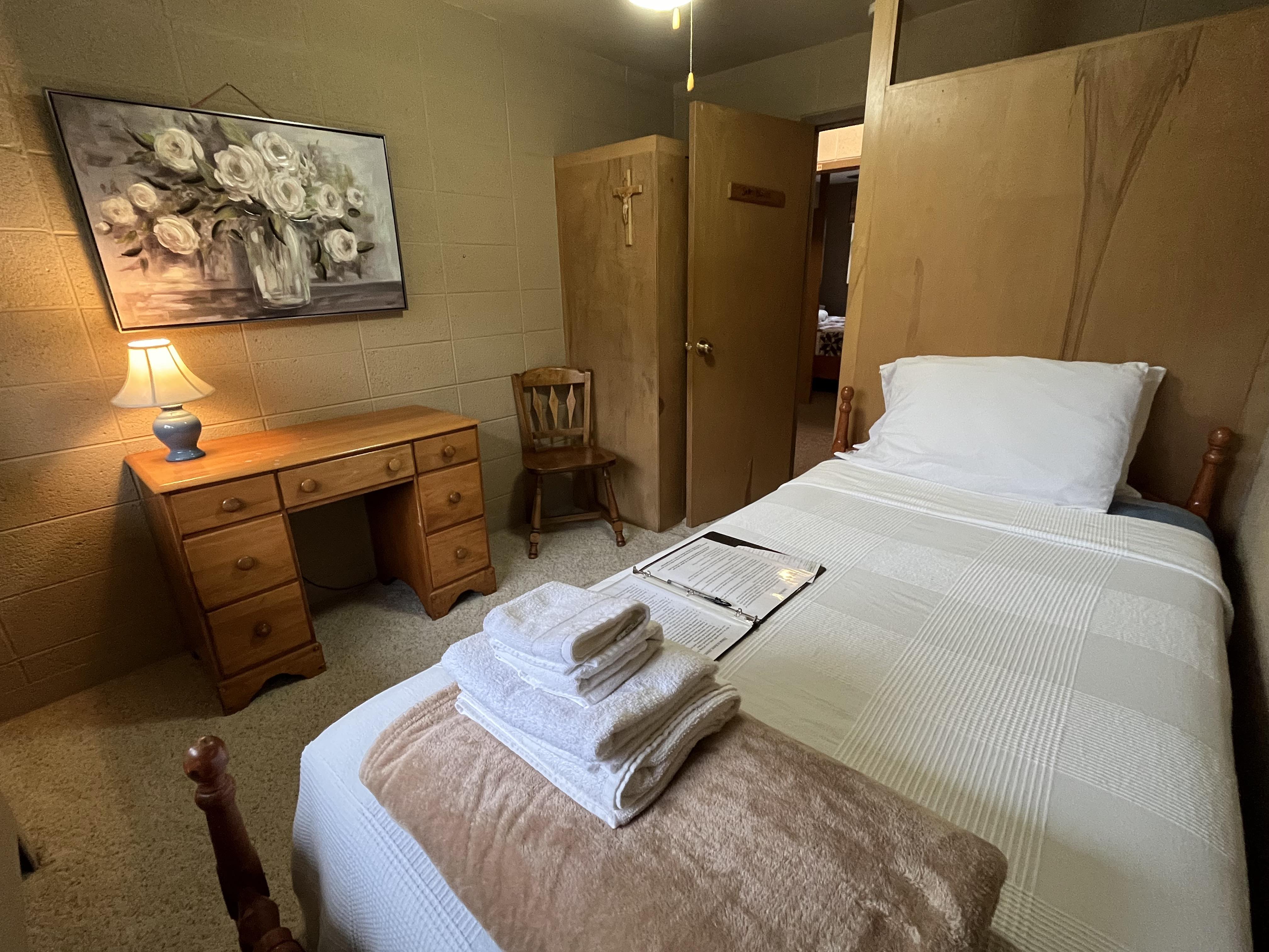 East Wing room with single bed, writing desk, and crucifix